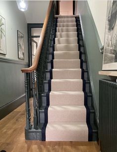 the stairs are lined with pink carpet and black iron railings, along with pictures on the wall