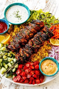 a plate full of food including meat, rice and veggies with dipping sauces