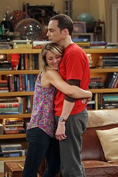 the young man and woman are hugging each other in front of a bookshelf