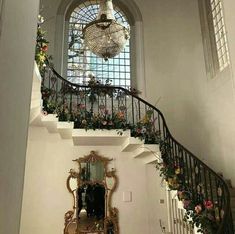 a staircase with flowers on the railing and a chandelier hanging from the ceiling