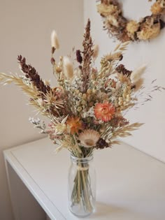 a vase filled with lots of flowers sitting on top of a white table next to a wreath