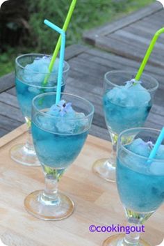 three glasses filled with blue liquid and straws sitting on a cutting board next to each other