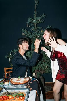 a man feeding a woman cake at a party by a christmas tree in the background