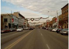 cars are parked on the street in front of buildings with christmas lights strung over them