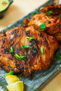 two pieces of chicken on a plate with lemon wedges and cilantro garnish