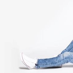 a man sitting on the floor with his legs crossed and wearing blue jeans, white sneakers