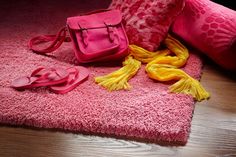 pink and yellow items are laying on the floor next to a pillow, bag, and slippers