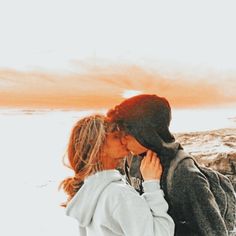 two people standing next to each other in front of an orange and white sky with clouds