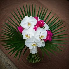 a bouquet of white and pink flowers sitting on top of a wooden table next to palm leaves