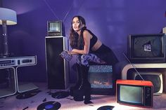 a woman sitting on the floor in front of some old televisions