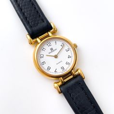 Vintage ladies' Givenchy gold-plated watch with round white dial and black leather strap. A gorgeous watch from the French designer. Quartz mechanism. Battery fitted, working perfectly. Width: 2,2cm (Will fit a wrist up to 17,1cm) The watch itself is in excellent cosmetic condition overall, with a scratch-free glass. The original leather strap is quite worn but still usable. Please see the pictures. --- Follow us on Instagram @finchleywatches Gold Plated Watch, Leather Strap Watch, French Designer, Women Wrist Watch, White Dial, Wrist Watches, Bling Bling, Vintage Watches, Quartz Watch