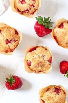 strawberry muffins with fresh strawberries scattered around them on a white countertop