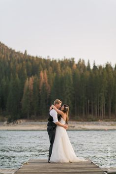 a bride and groom standing on a dock by the water