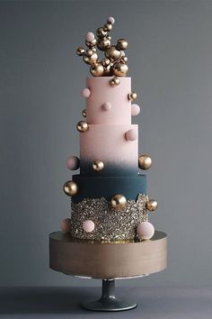 a multi - tiered cake with pink, blue and gold decorations sits on a metal stand