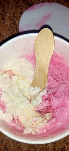 a white bowl filled with pink ice cream and a wooden spoon in it on top of a counter