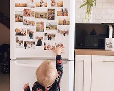 a little boy that is standing in front of a refrigerator with pictures on the door