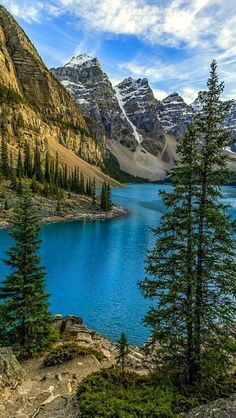 a mountain lake surrounded by pine trees and snow capped mountains in the distance with blue water