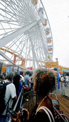 people are standing in front of a ferris wheel at an amusement park or fairground