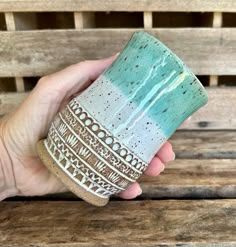 a hand holding a ceramic cup on top of a wooden bench