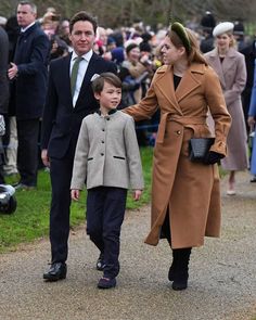 a man and woman walking down a path with a young boy in a suit on the other side