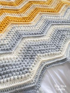 a crocheted blanket with yellow and gray stripes on it, sitting on a bed