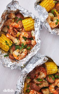 three foil packets filled with shrimp and corn on the cob