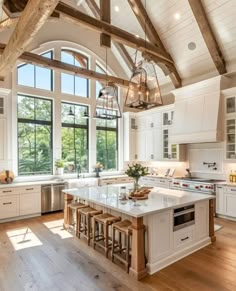 a large kitchen with white cabinets and an island in front of two windows that look out onto the woods