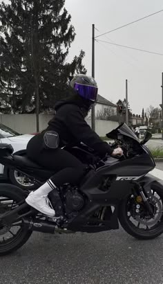 a man riding on the back of a motorcycle down a street next to parked cars