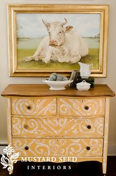 a painting on the wall above a dresser with a cow sitting on it's side