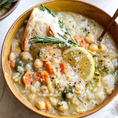 a bowl filled with soup and topped with lemon wedges, garnished with fresh herbs