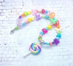 a candy beaded necklace with a lollipop charm on a white brick wall