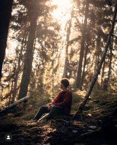 a man sitting in the middle of a forest looking up at the sun shining through the trees