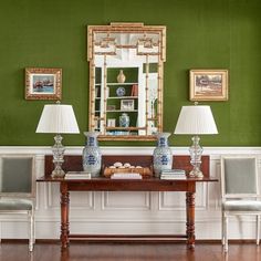 a room with green walls and two lamps on top of a table in front of a mirror