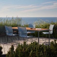 a wooden table surrounded by blue chairs on a deck next to the ocean with tall grass