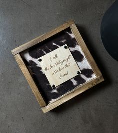 a wooden frame with a quote in it on the floor next to a black and white cow print rug