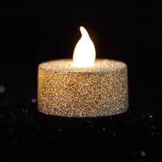 a lit candle sitting on top of a black surface with lots of glitter around it