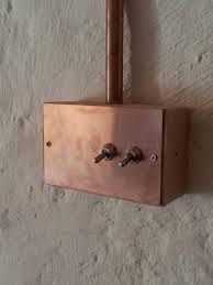 a copper light switch mounted to the side of a white wall with metal fittings