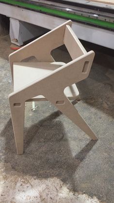 an unfinished chair sitting on the ground in front of a table with a machine behind it