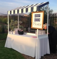 a man standing next to a white table covered in flowers and plants with a sign that reads boot beer floats