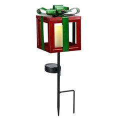 a red and green lantern on a stand with a lit candle in the center that is attached to it