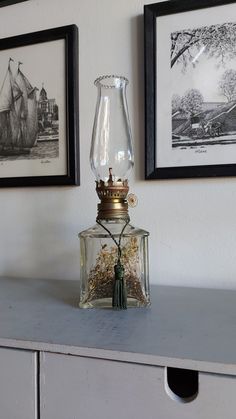 a glass lamp sitting on top of a dresser next to two framed pictures above it