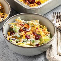 two bowls filled with food next to silverware on a marble counter top and one bowl has salad in it