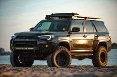 a black toyota truck parked on top of a beach next to the ocean at sunset