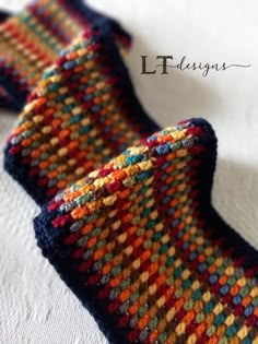 two knitted ties sitting on top of a white cloth covered in multicolored yarn