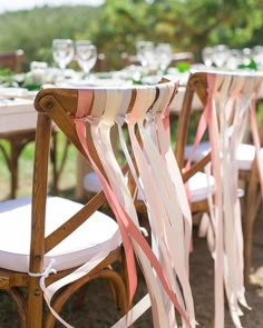 the chairs are lined up with ribbons and wine glasses on top of each chair for an outdoor wedding reception