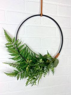 a fern wreath hanging on a brick wall with black leather cord and wooden handles for decoration