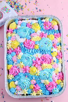 a cake with blue, yellow and pink frosting in a pan on top of confetti sprinkles