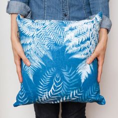 a woman holding a blue pillow with white fern leaves on it, in front of her