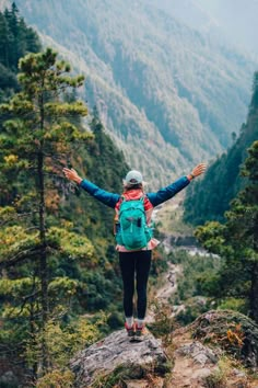 a woman standing on top of a mountain with her arms outstretched in the air while wearing a backpack