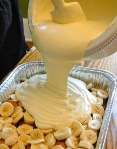 a pan filled with bananas and cream being drizzled on top of it